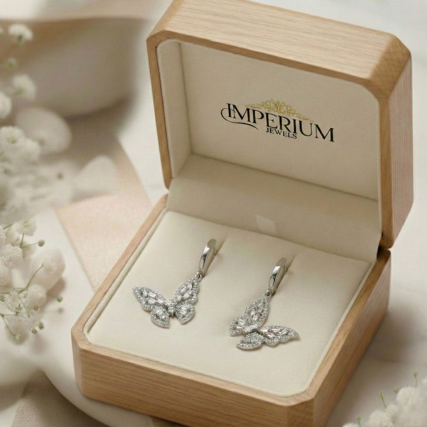 Butterfly-shaped earrings in a 'Imperium Jewels' box with white flowers in the background