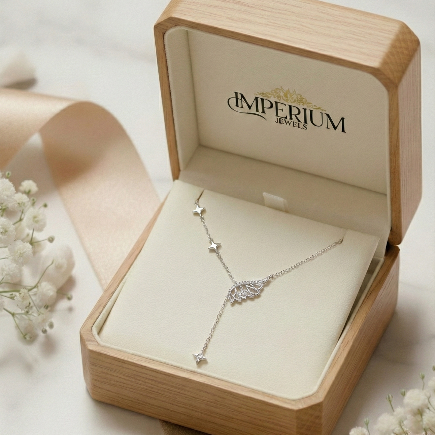 Silver necklace in an open jewelry box with 'Imperium Jewels' branding, surrounded by white flowers.