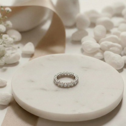 Silver ring on a marble surface with flowers and pebbles in the background