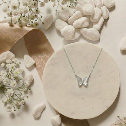 Butterfly necklace on a marble surface with pebbles and small white flowers