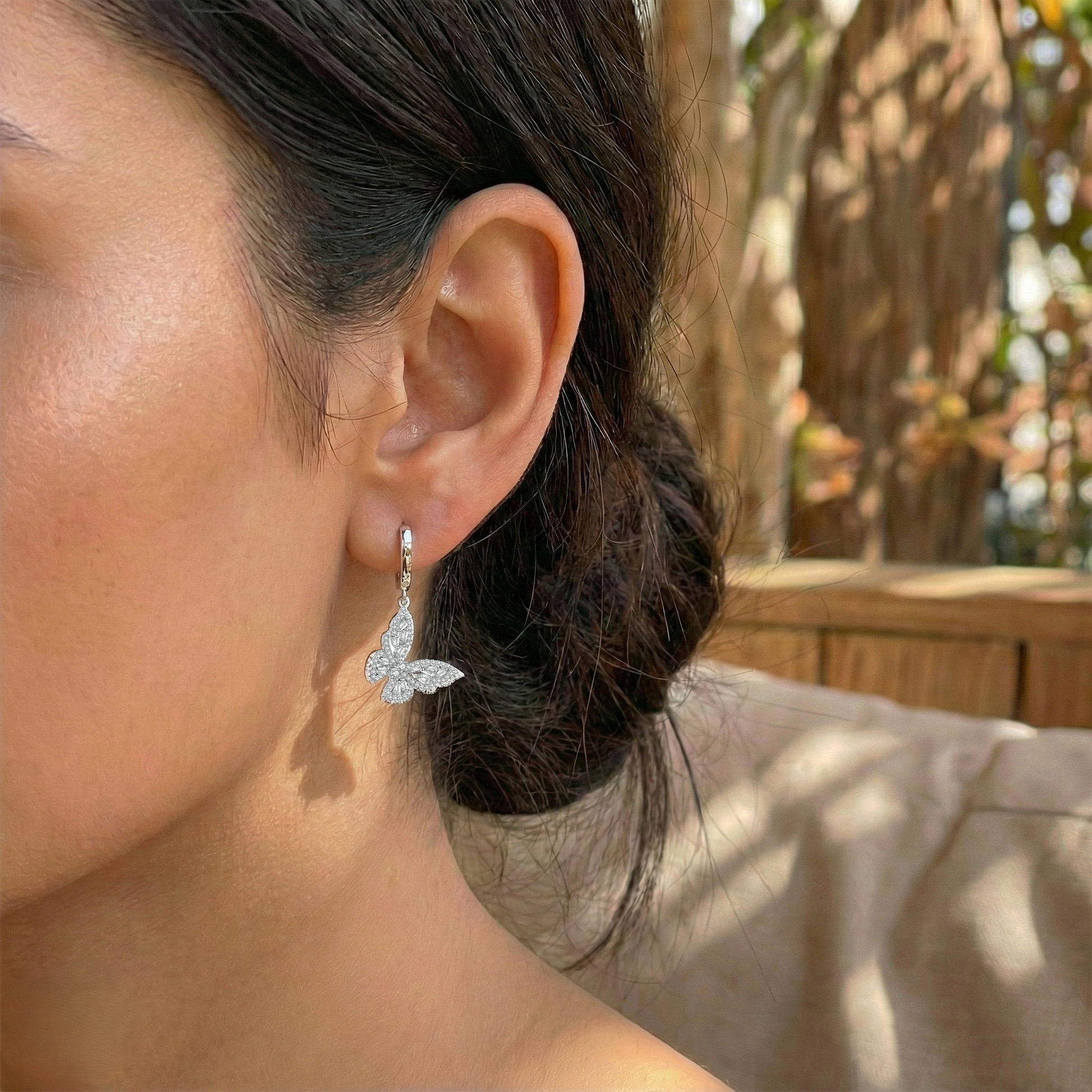 Close-up of a person wearing a butterfly-shaped earring outdoors.