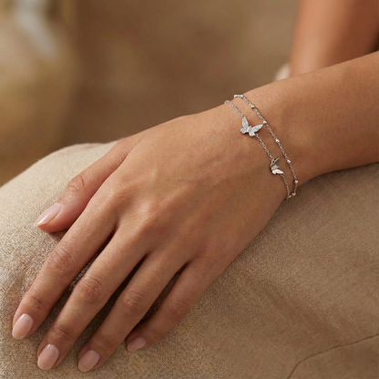 Hand wearing a delicate silver bracelet with butterfly designs on a beige surface