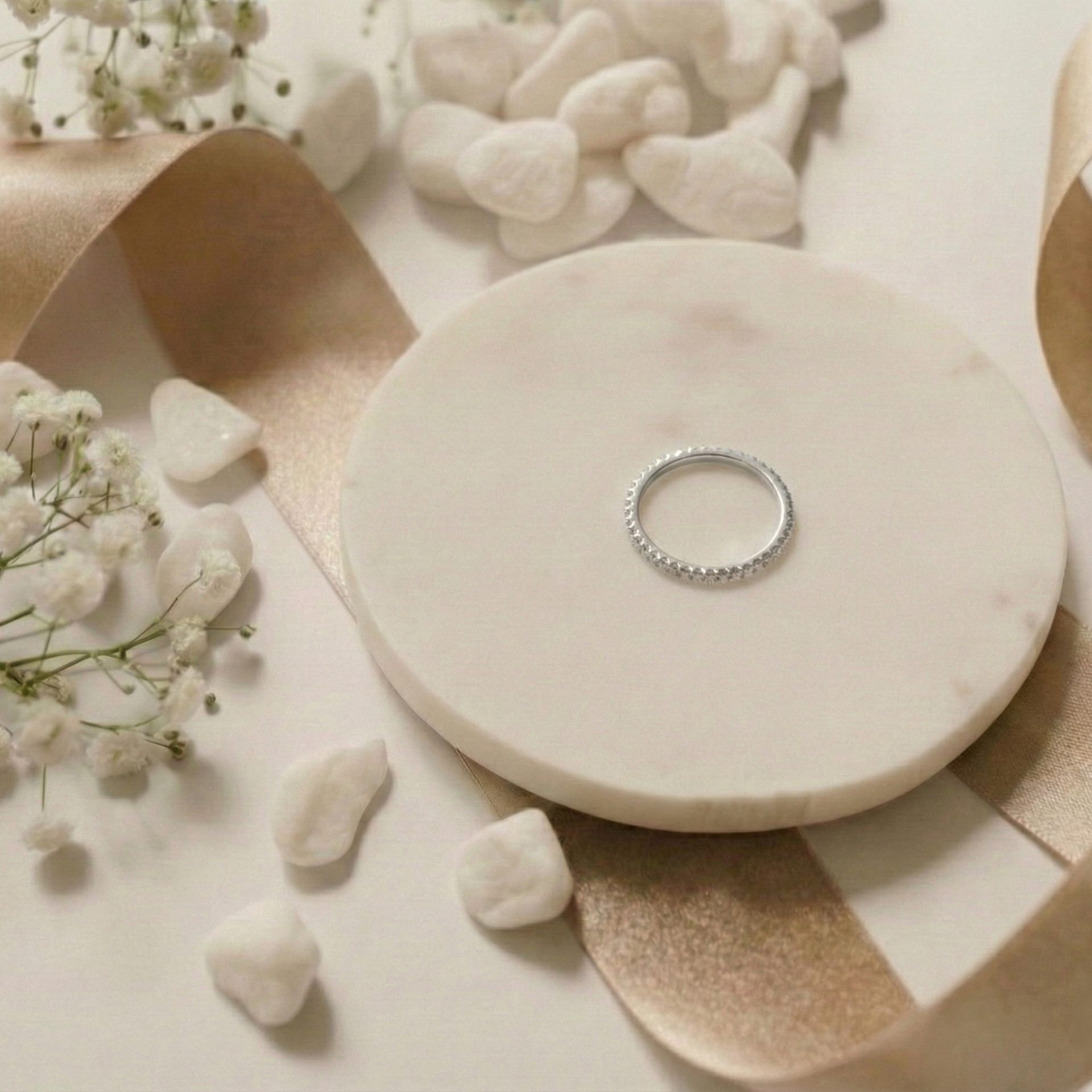 Silver ring on a marble surface with small stones and flowers
