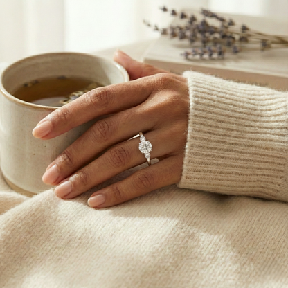 Hand wearing a ring with a diamond, holding a cup of tea on a soft surface.