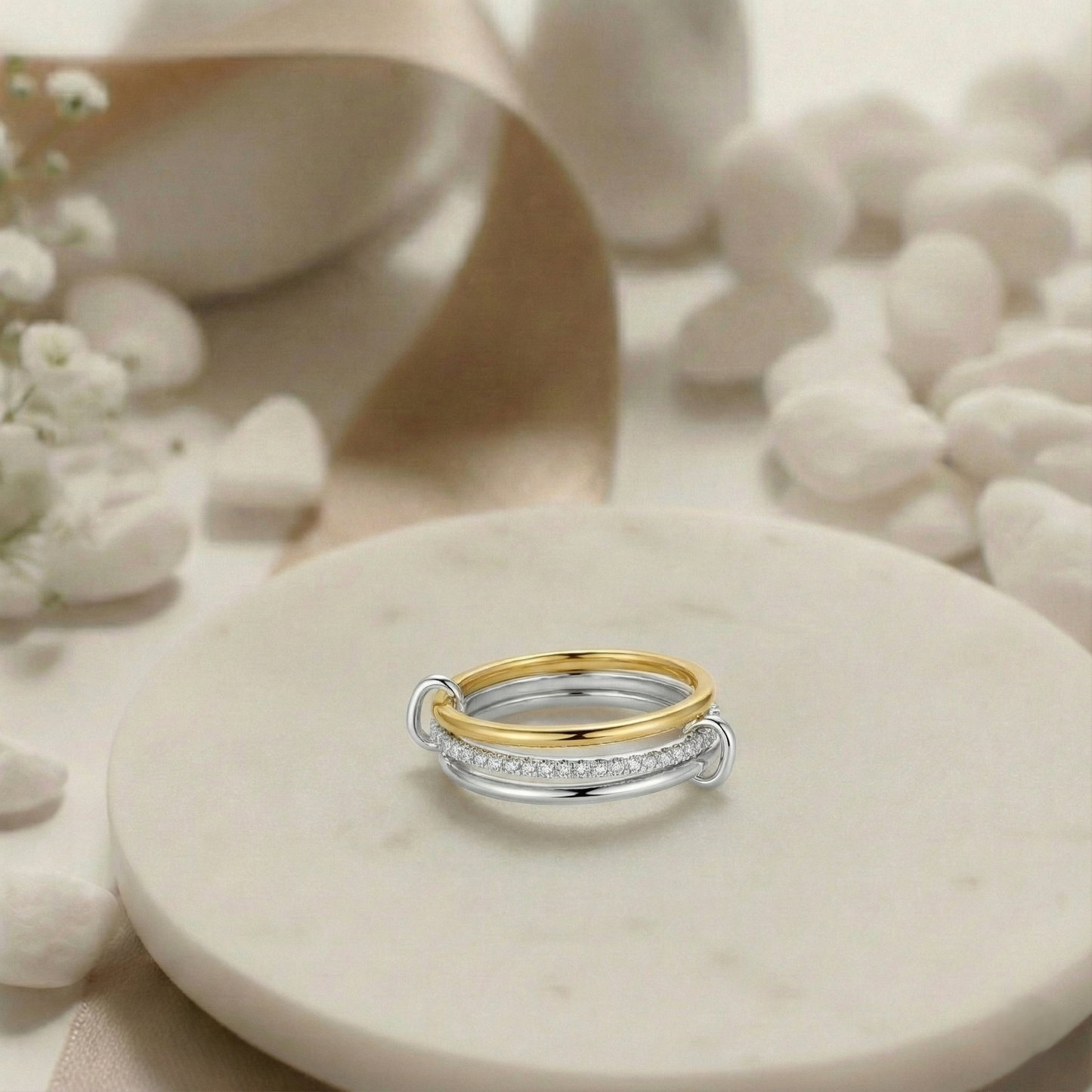 Two gold and silver rings on a beige stone surface with white flowers.