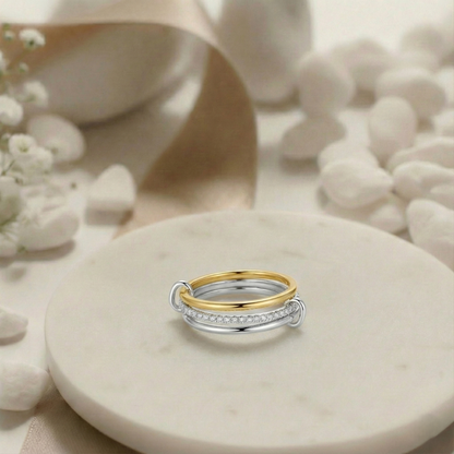 Two gold and silver rings on a beige stone surface with white flowers.
