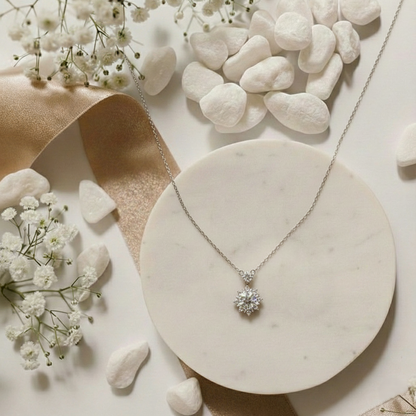 Silver necklace with a diamond pendant on a marble surface with white flowers and stones.
