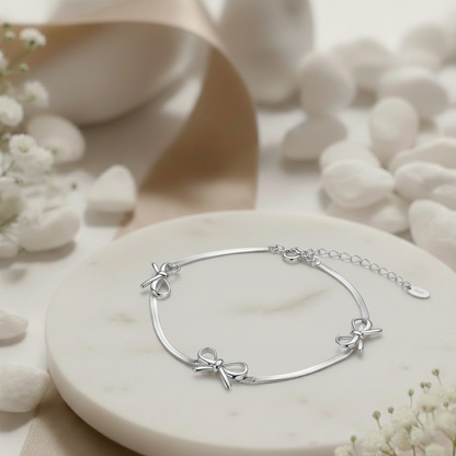 Silver bracelet with bow details on a white stone surface with flowers
