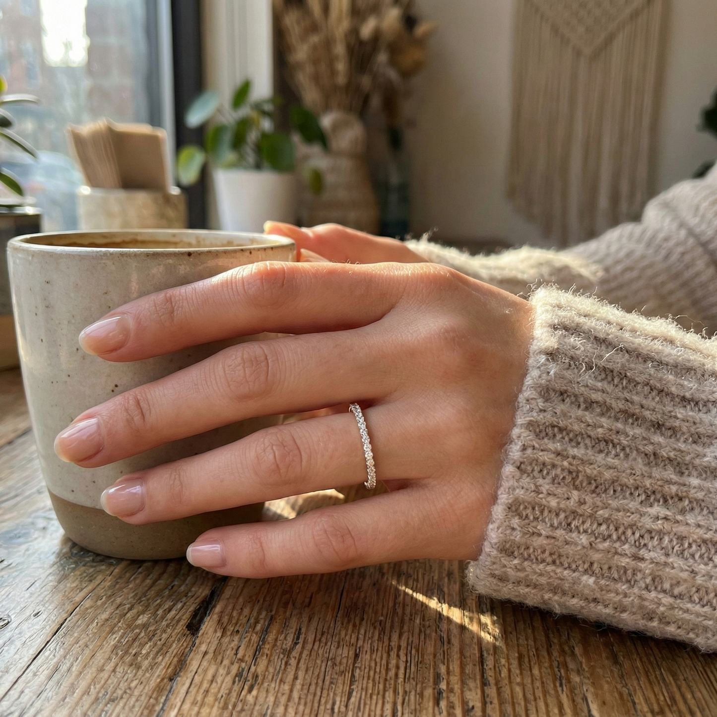 Hand holding a ceramic mug on a wooden surface with a cozy indoor background