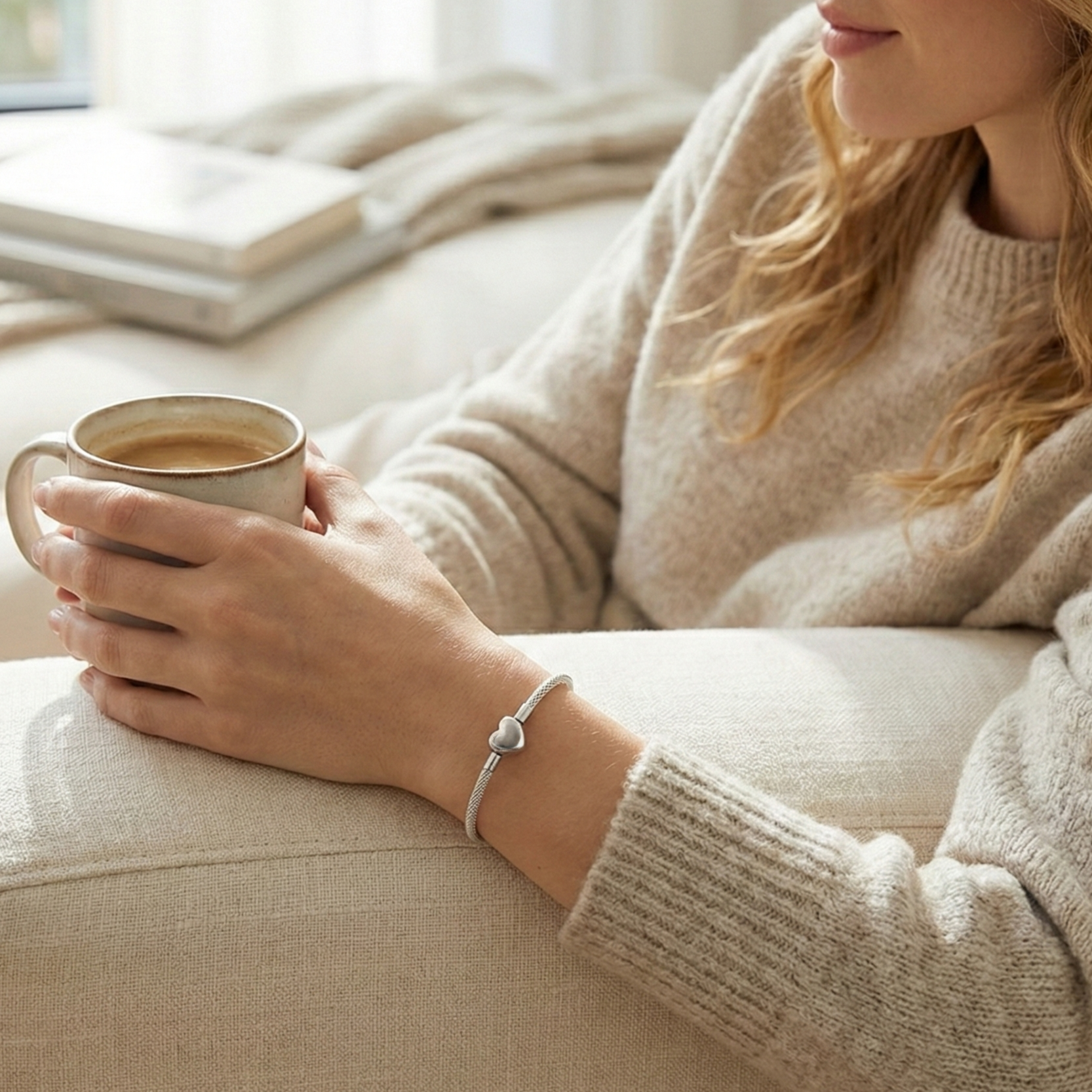Person holding a mug of coffee on a couch wearing a silver bracelet