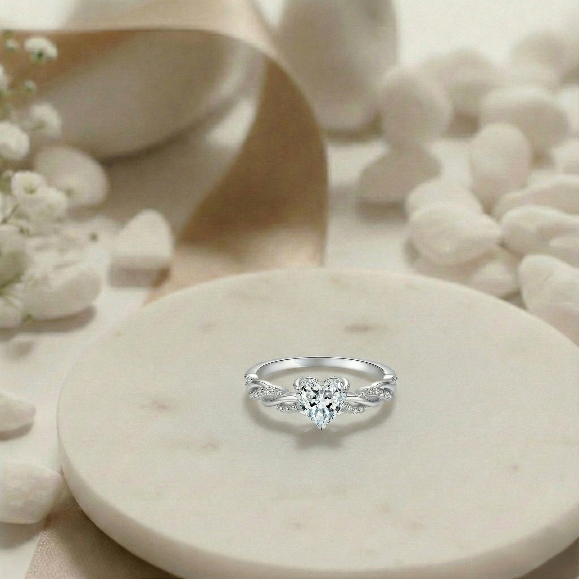 Silver ring with a heart-shaped center stone on a marble surface with flowers.
