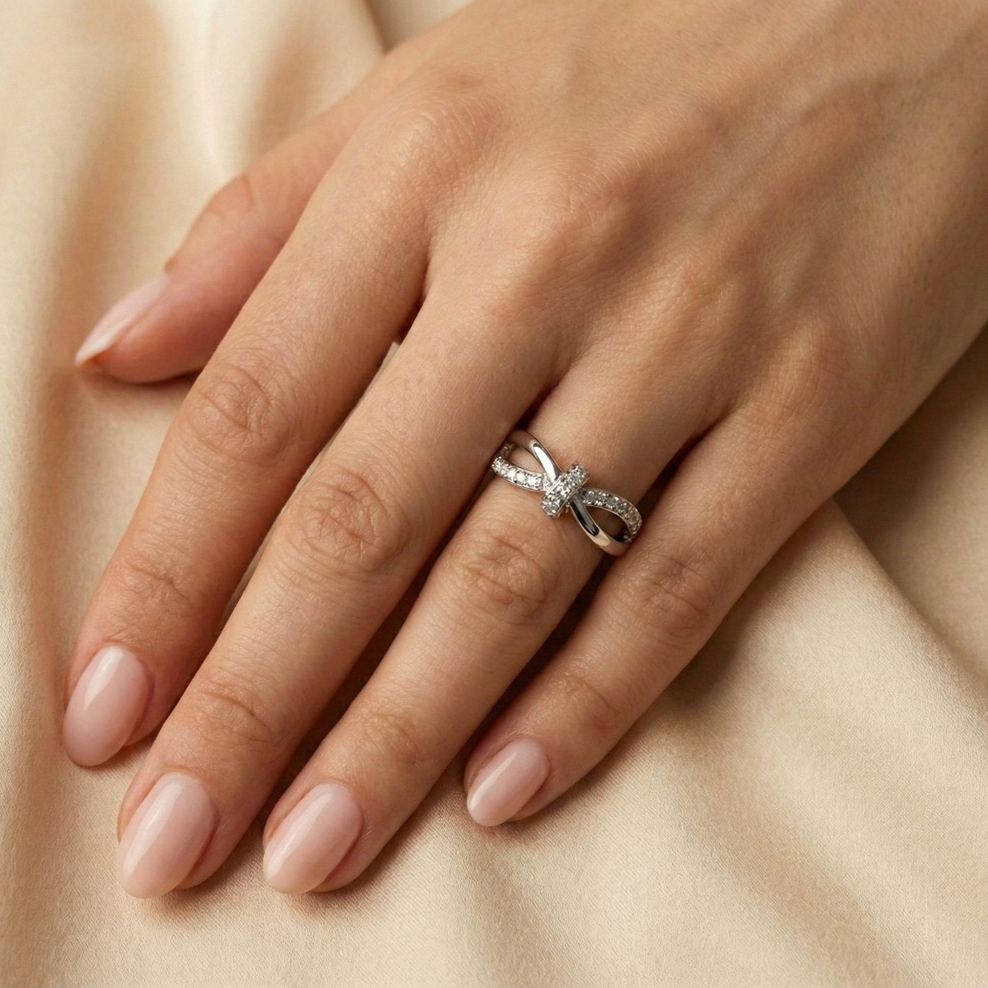 Hand wearing a silver ring with a bow design on a beige fabric background