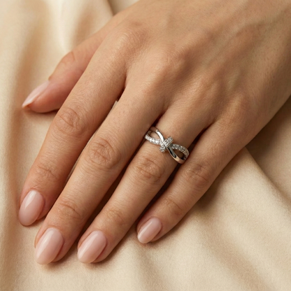 Hand wearing a silver ring with a bow design on a beige fabric background
