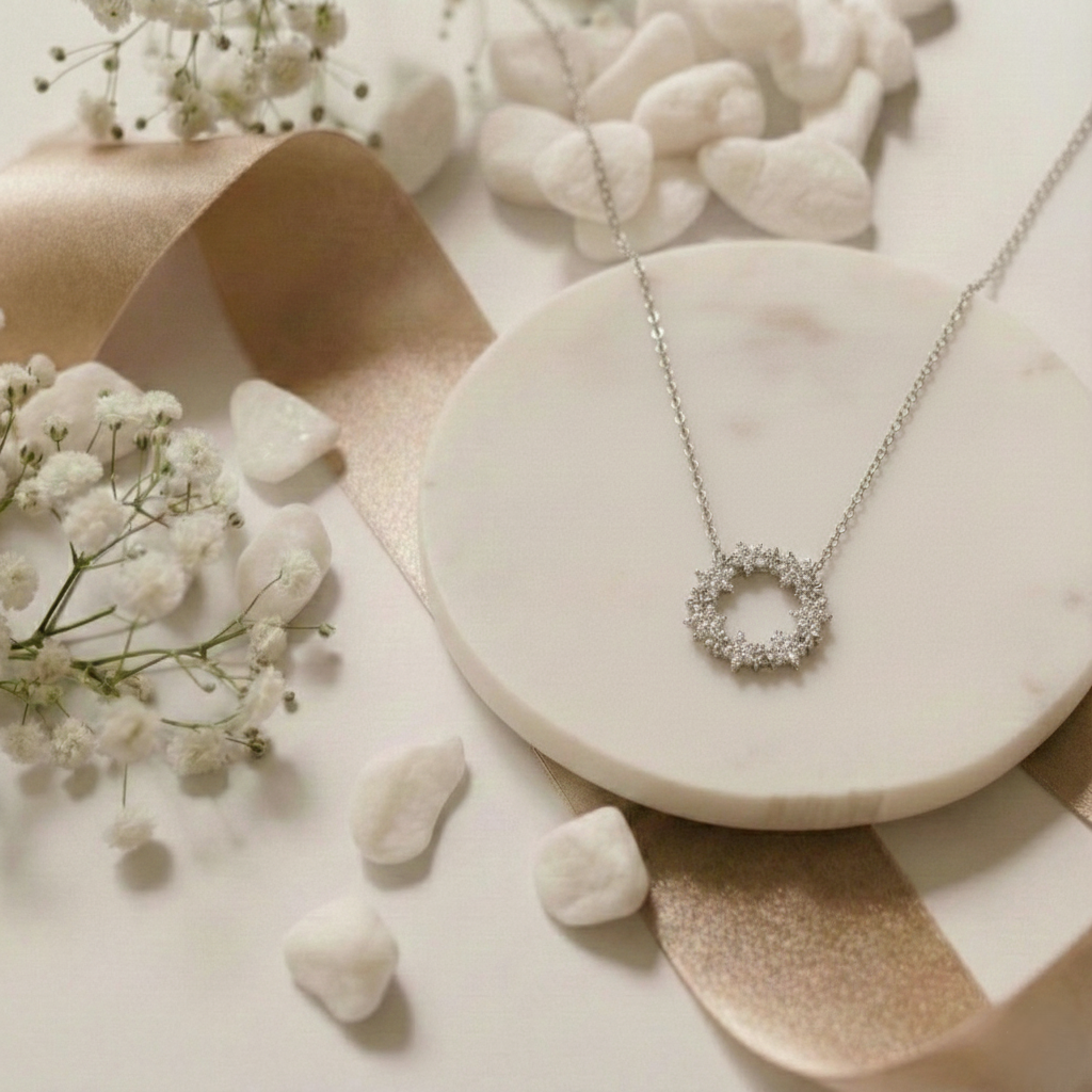 Silver necklace with a circular pendant on a marble surface with small white flowers and stones.