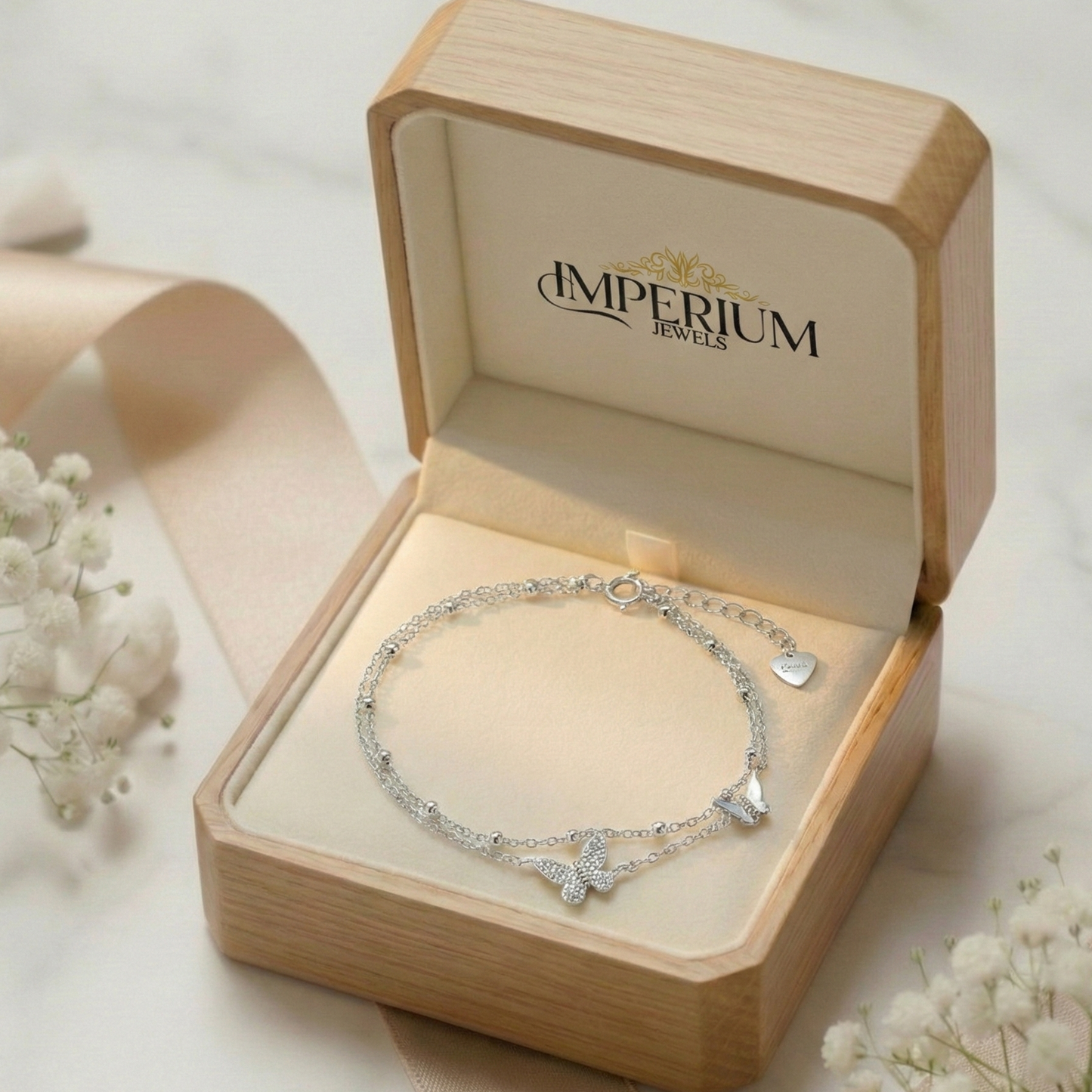 Silver bracelet in an open wooden box with 'Imperium Jewels' branding, surrounded by delicate flowers.