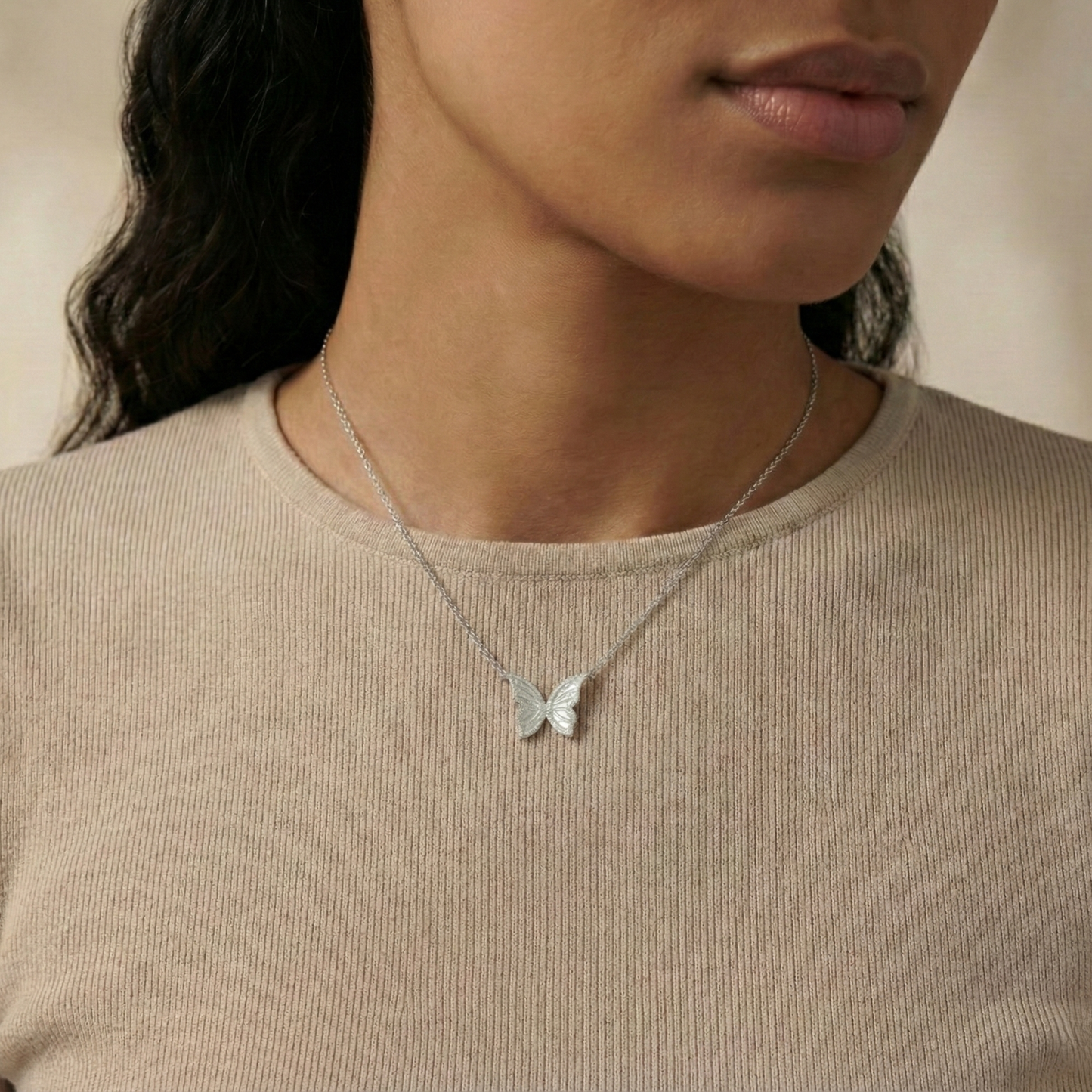 Butterfly necklace worn by a person against a neutral background