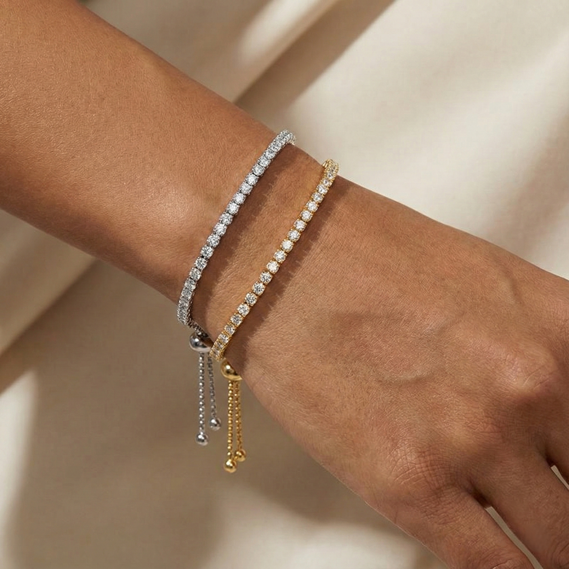 Close-up of a wrist wearing three delicate bracelets on a neutral background