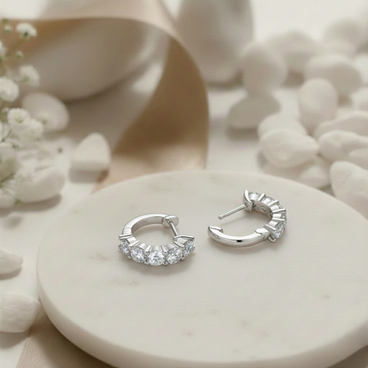 Silver hoop earrings on a white stone surface with delicate flowers in the background
