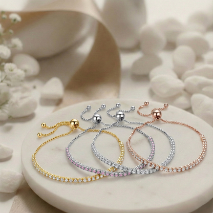 Four bracelets in gold, silver, and rose gold on a white stone surface with flowers.