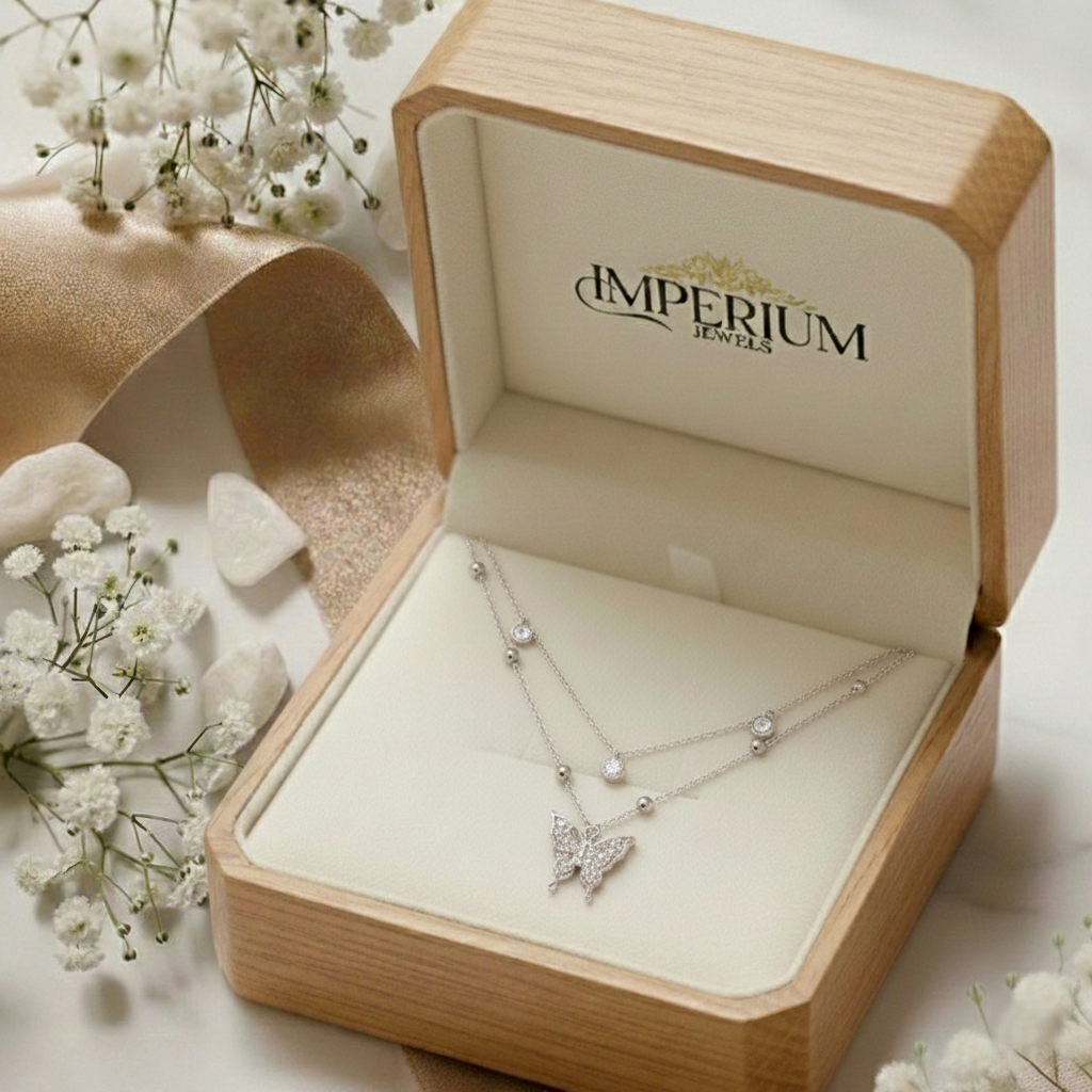 Butterfly necklace in a wooden jewelry box with 'Imperium Jewels' branding, surrounded by white flowers.