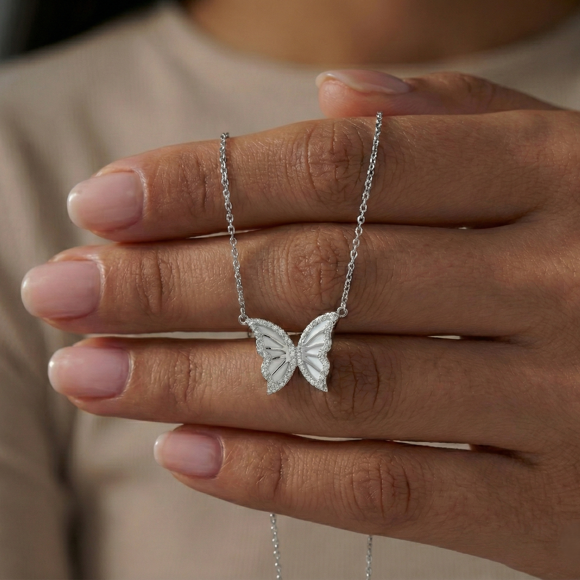 Silver butterfly necklace held between fingers against a neutral background