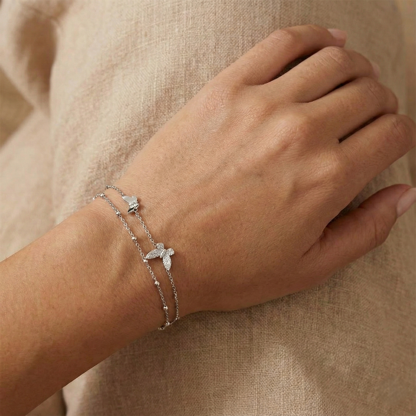 Hand wearing a silver bracelet with butterfly charm on a beige background