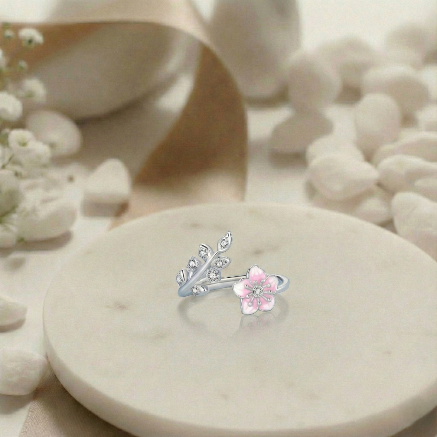 Silver and pink floral earring on a white stone surface with flowers in the background