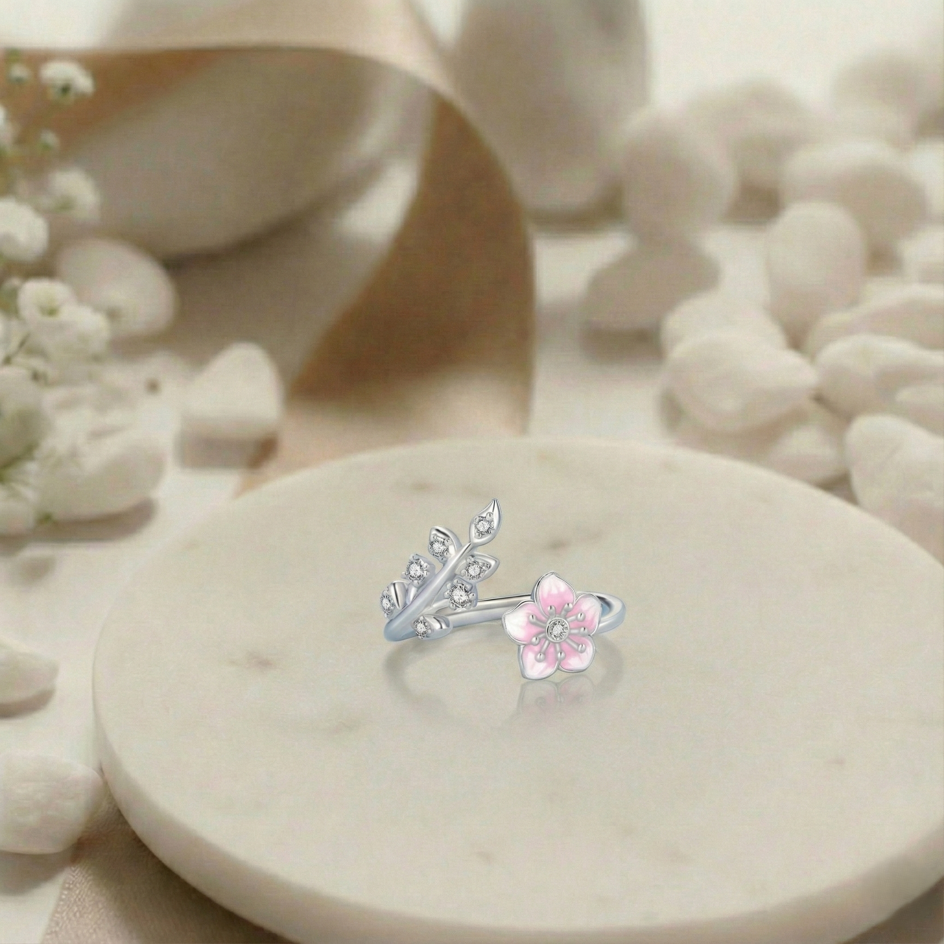 Silver and pink floral earring on a white stone surface with flowers in the background