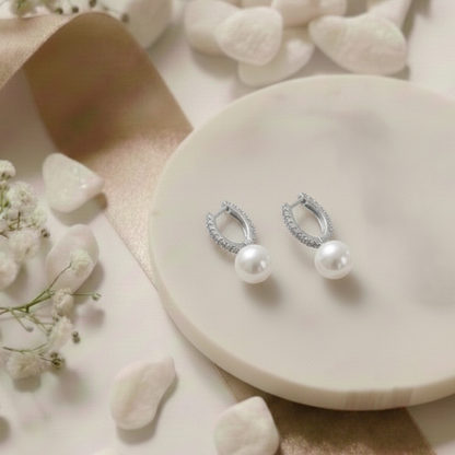 Pair of pearl earrings on a white stone surface with small flowers.