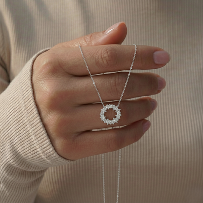Hand holding a silver necklace with a circular pendant against a neutral background
