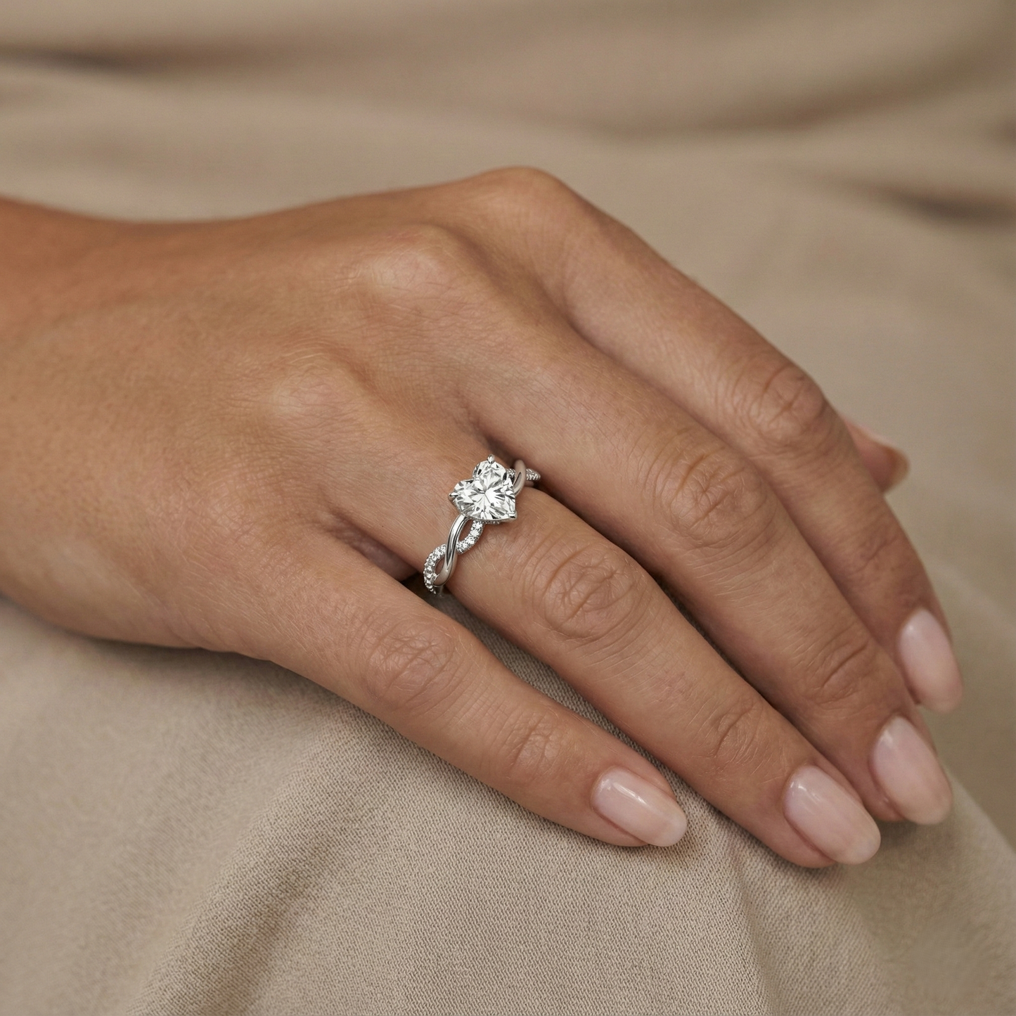 Close-up of a hand wearing a silver ring with a diamond on a beige fabric background