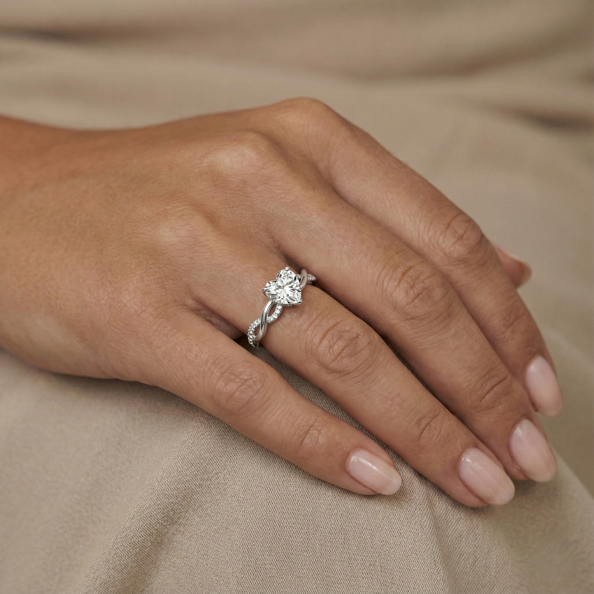 Close-up of a hand wearing a silver ring with a diamond on a beige fabric background