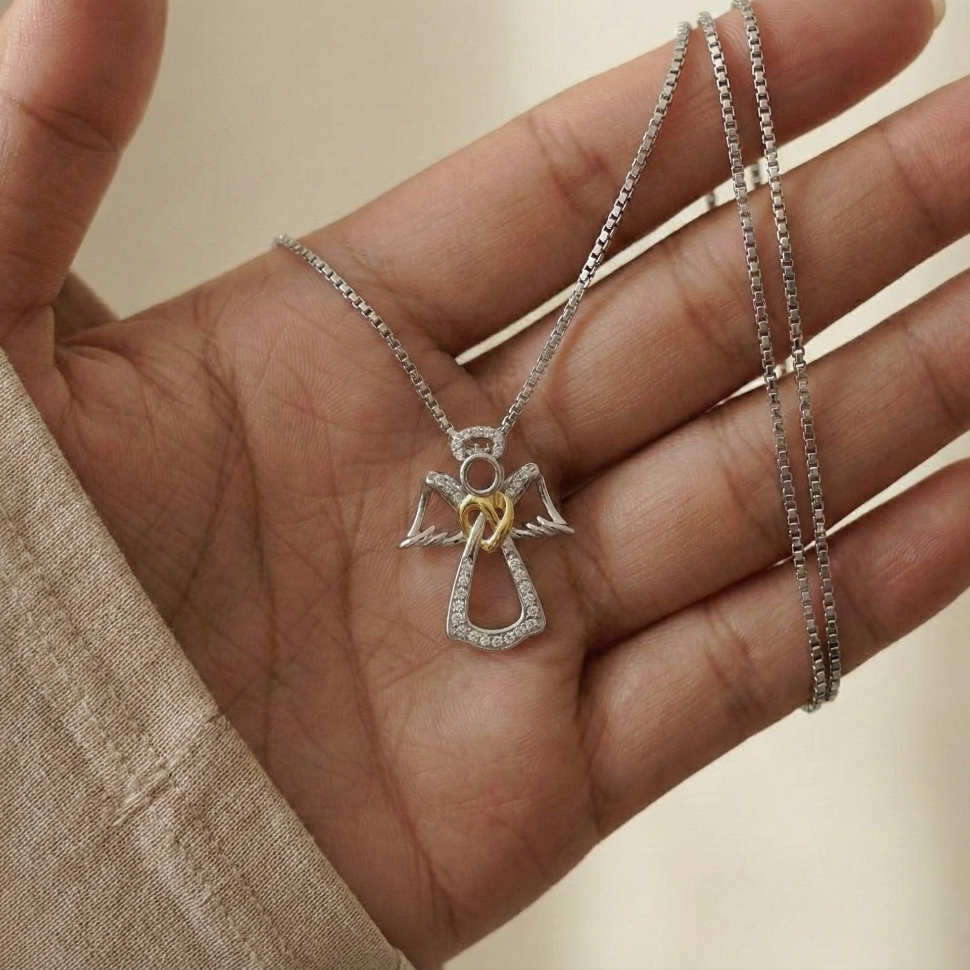 Silver necklace with an angel pendant held in a hand against a neutral background