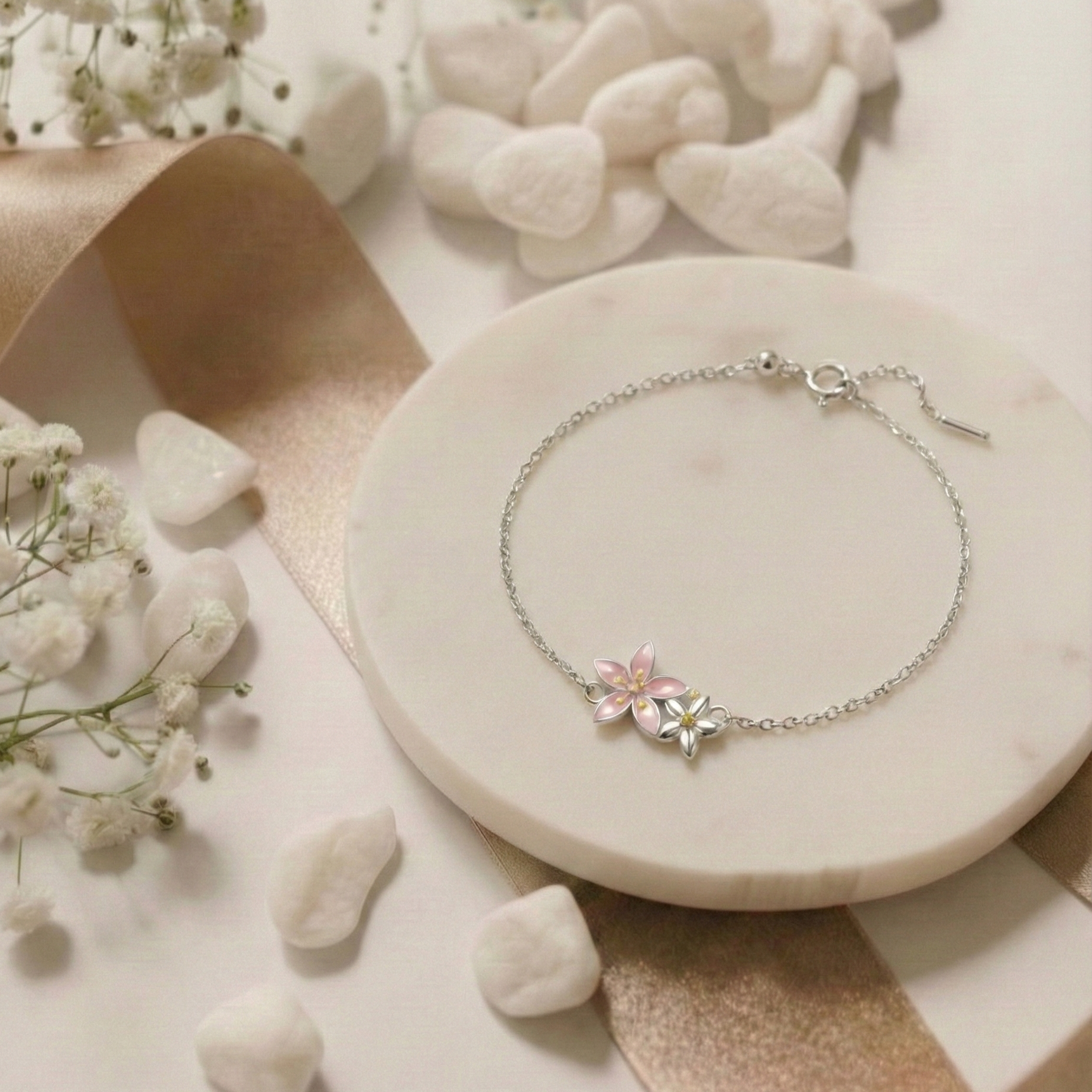 Silver bracelet with floral charm on a marble surface with flowers and stones.