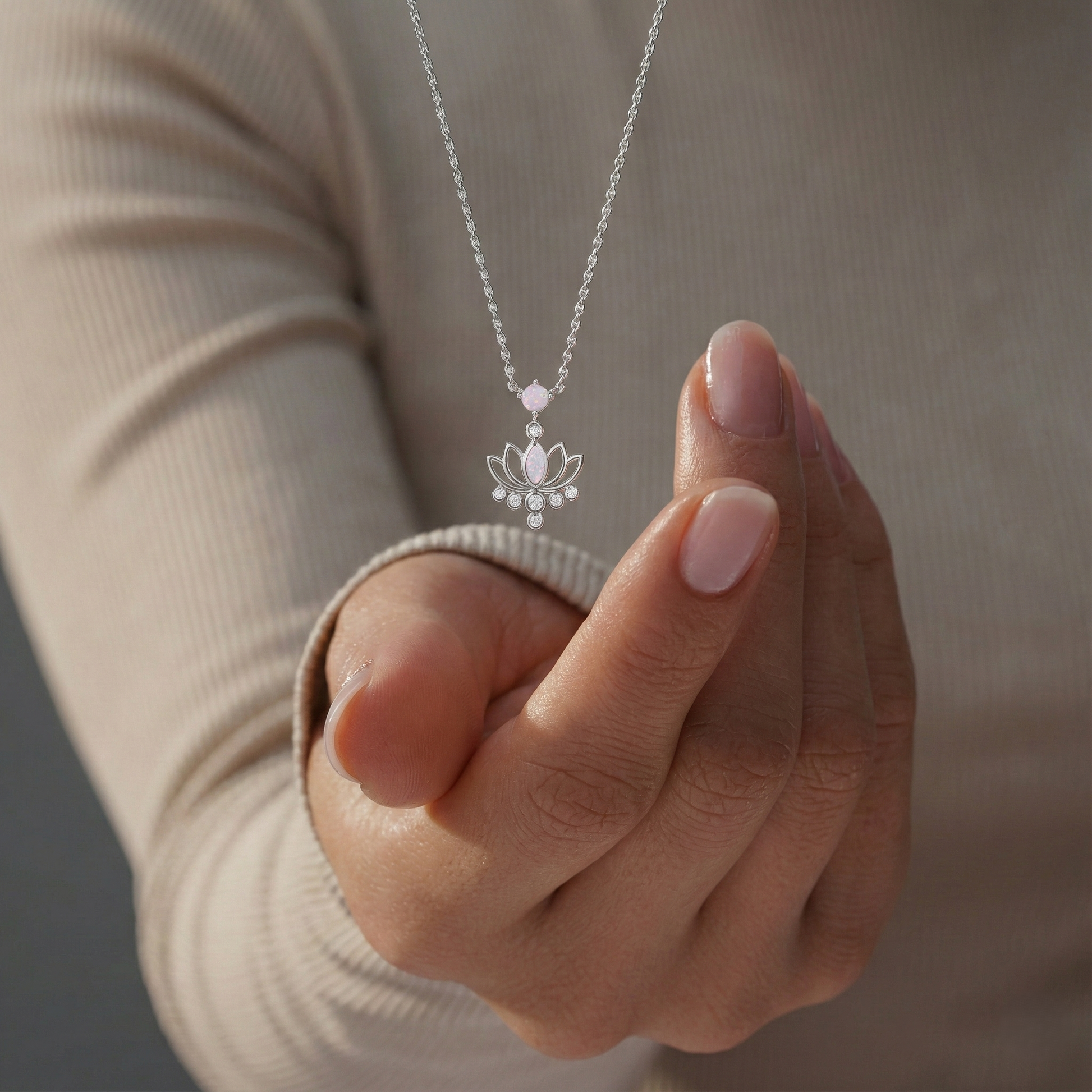 Hand holding a silver necklace with a lotus flower pendant against a neutral background