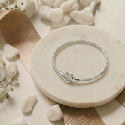 Silver bracelet with a heart charm on a stone surface with white flowers