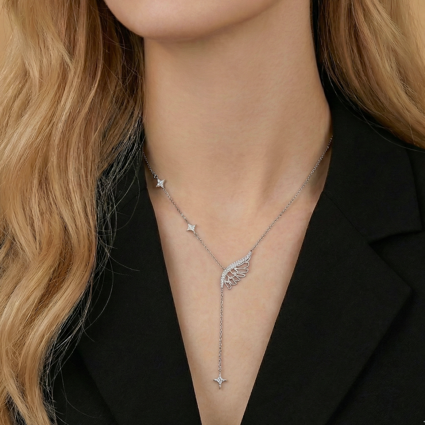 Silver necklace with a wing pendant worn by a person with blonde hair.