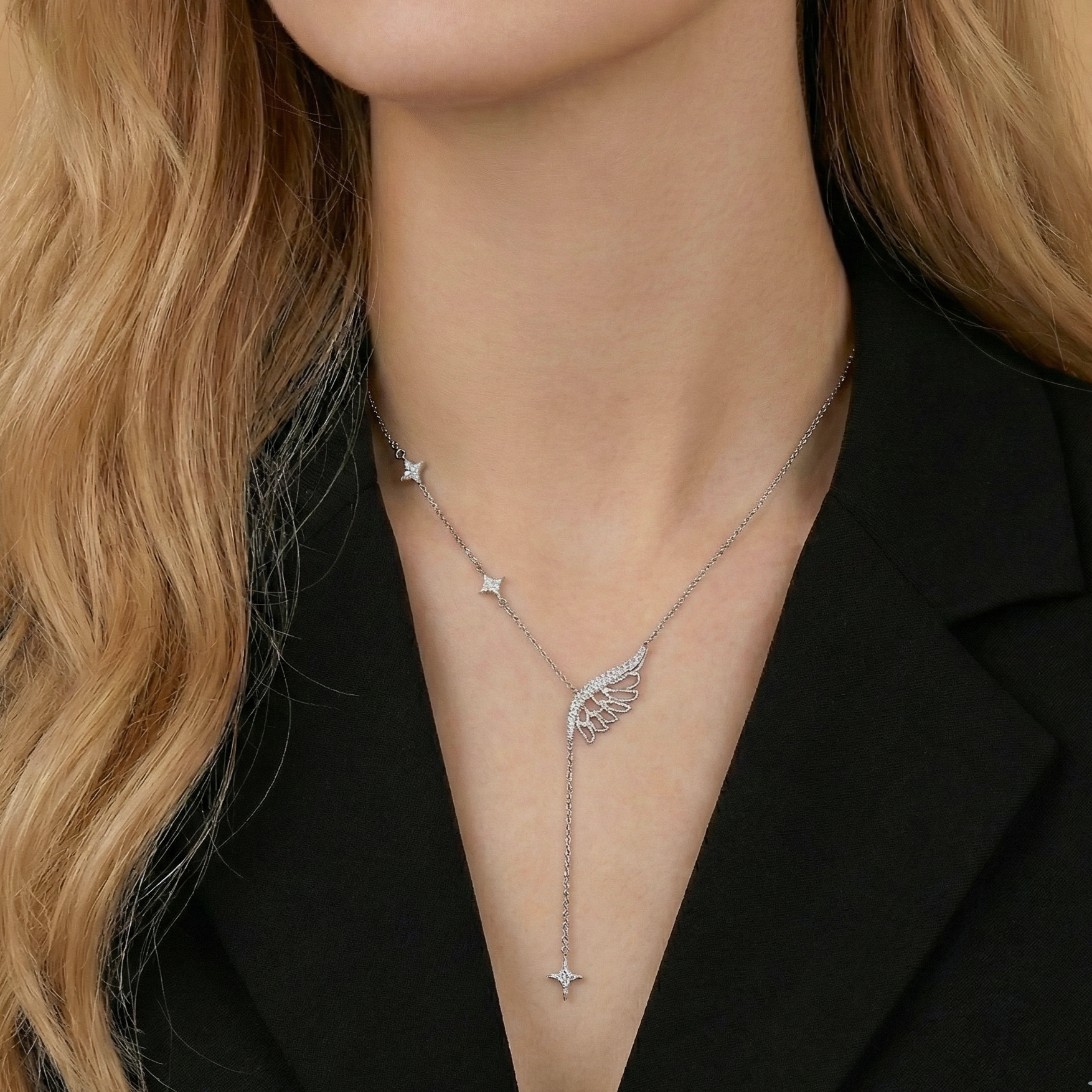 Silver necklace with a wing pendant worn by a person with blonde hair.