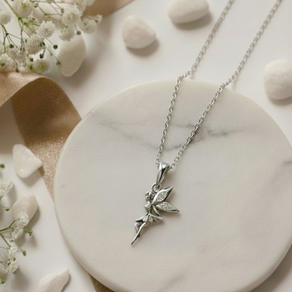 Silver necklace with a fairy pendant on a white dish with flowers and stones.