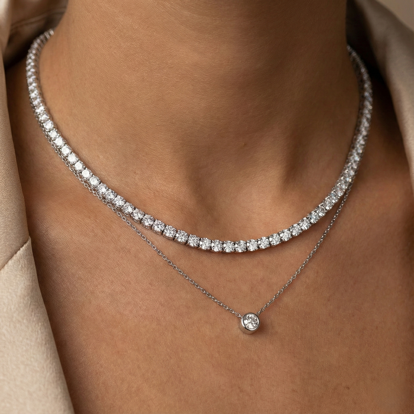Close-up of a person wearing two diamond necklaces on a neutral background