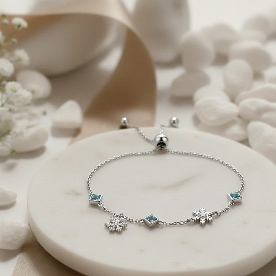 Silver bracelet with snowflake and gemstone charms on a white stone surface with flowers.