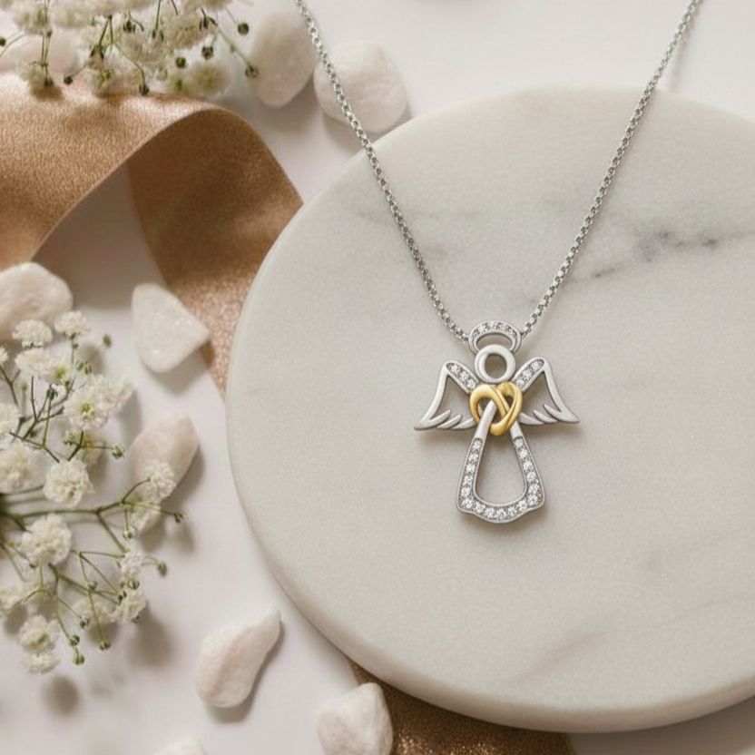 Silver angel necklace with a gold heart on a marble surface with flowers