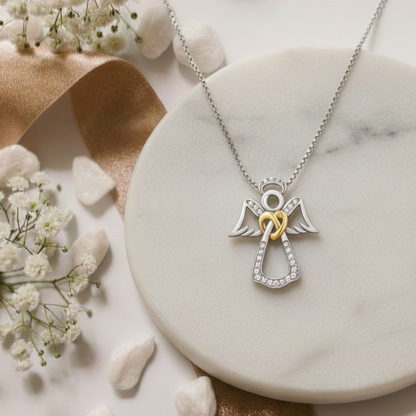 Silver angel necklace with a gold heart on a marble surface with flowers