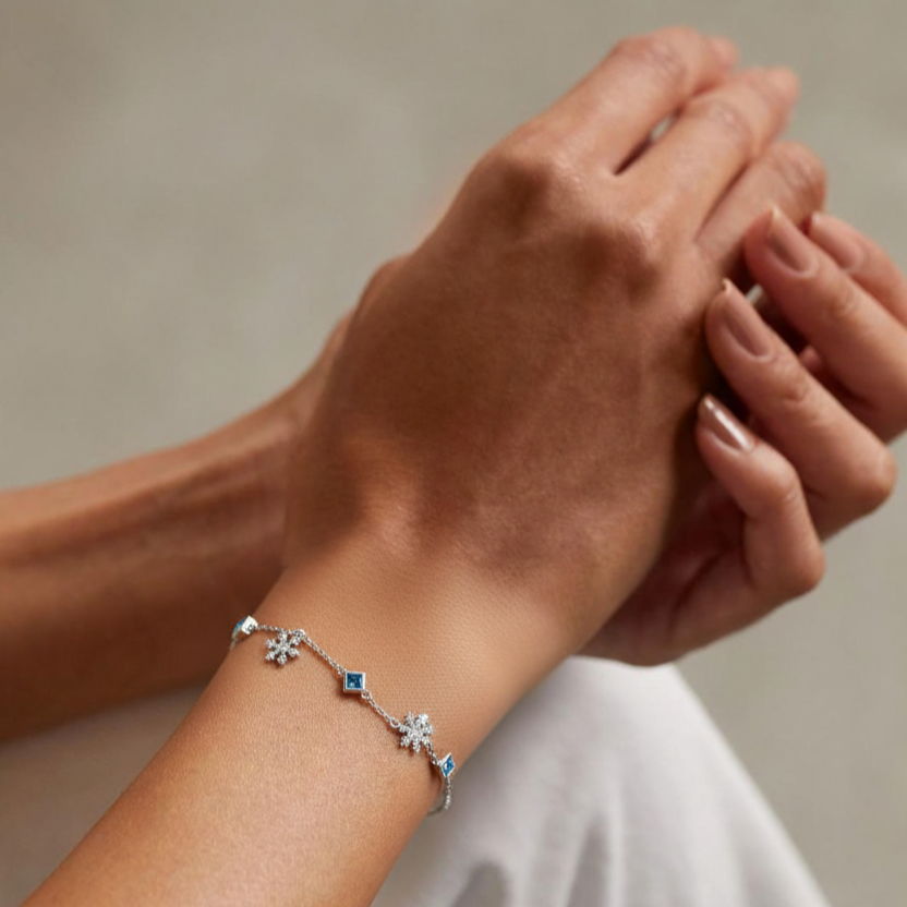 Close-up of a hand wearing a silver bracelet with blue stones on a neutral background
