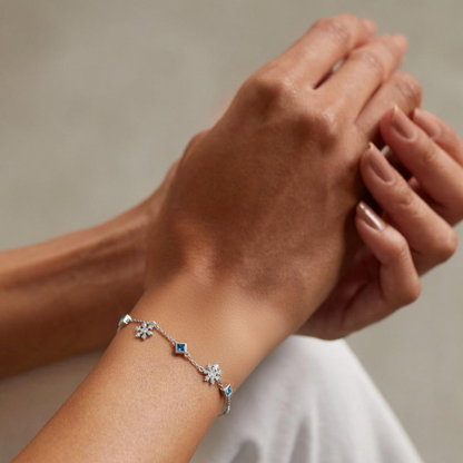Close-up of a hand wearing a silver bracelet with blue stones on a neutral background