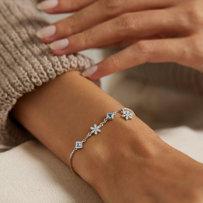 Close-up of a hand wearing a silver bracelet with blue stones on a neutral background